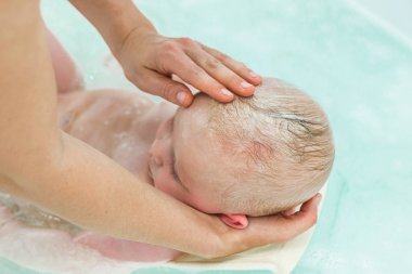 6 aylık erkek bebek banyo. Küçük çocuk bir küvet içinde. Bebek yıkama ve banyo. Tanınmayan anne bebeğini banyo.
