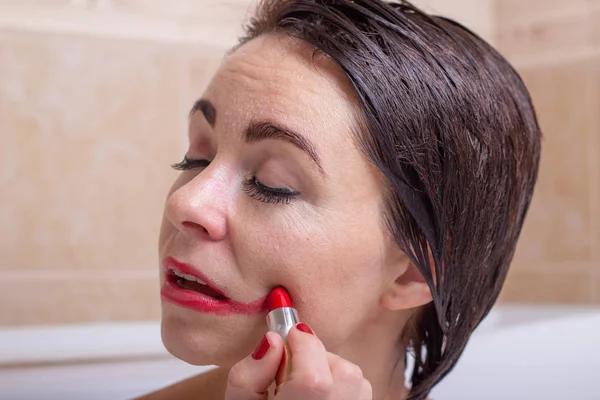 female depression. a woman in the bathroom with a petrified look slashes lipstick on her face.