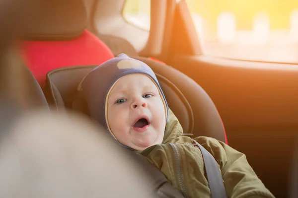 Close Up caucasian cute baby boy woke up and yawns in modern car seat. Child traveling safety on the road. Safe way to travel fastened seat belts in a vehicle with young kids. Trip with toddler. — Stock Photo, Image
