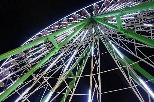 Et pariserhjul snur seg om kvelden i mørket. Hjulet er lyst hvitt. diagonalt sett nedenfra . – stockfoto
