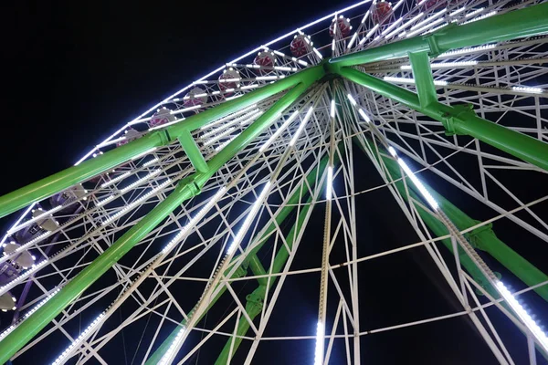 Una rueda de la fortuna gira en la noche en la oscuridad. La rueda está iluminada de blanco. ver en diagonal desde abajo . — Foto de Stock