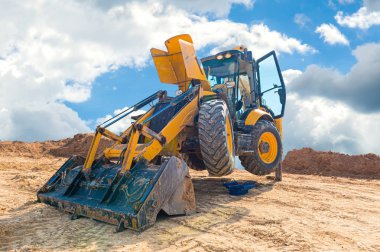 Mavi gökyüzüne karşı bir şantiyede sarı ekskavatör bakımı. hafriyat işleri sırasında kum havuzunda tekerlek yükleyicireni repearing