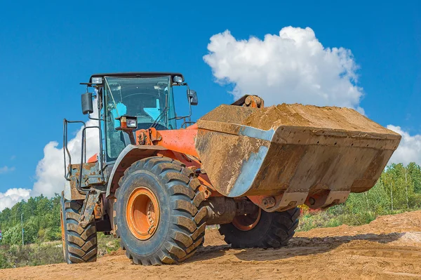Backhoe loader or bulldozer - excavator with clipping path on a background with blue sky and clouds. work on construction site or sand pit — Stock Photo, Image
