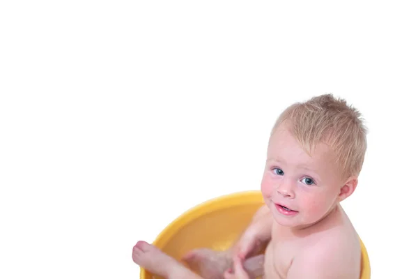 Bebé sentado en una bañera azul mirando hacia arriba, niño pequeño se sienta dentro de baño amarillo. niño en el lavabo tomando un baño — Foto de Stock