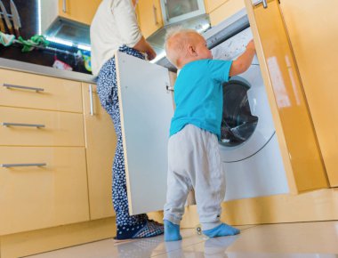 Onun moter mutfak işi yaparken çamaşır makinesi döngüleri ile ilgilenen bebek çocuk