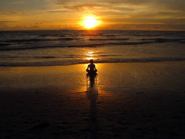 Молодая женщина сидит на пляже, силуэт на закате. Молодая женщина практикует йогу на открытом воздухе. Концепция гармонии и медитации. Здоровый образ жизни. медитировать на йоге лотоса — стоковое фото