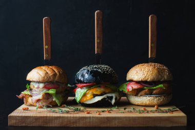 Ağaç yapımı lezzetli hamburgerler sığır eti burgeri ve taze sebzeler. Tahta üzerinde bıçaklarla servis ediliyor. Karanlık arka planda. Lezzetli yemek..