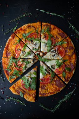 Geleneksel İtalyan pizzası. Dilimler halinde dilimlenmiş lezzetli taze pizza otlar ve peynirle koyu bir arka planda. Üst Manzara. Siyah masada pizza..