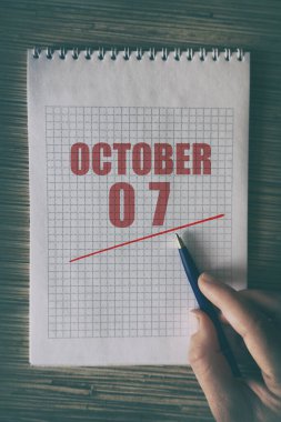 7 Ekim. Ayın yedinci günü, insan elini kırmızı altı çizili not defteriyle kapat. Sonbahar ayı, yılın günü konsepti..