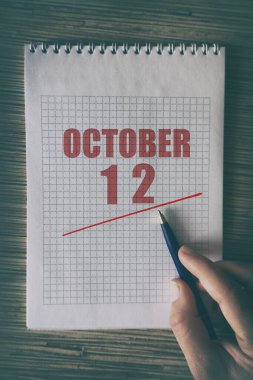 12 Ekim. Ayın 12 'sinde insan elini kırmızı altı çizili not defteriyle kapat. Sonbahar ayı, yılın günü konsepti..