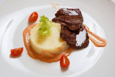 Kızarmış et dilimleri, lobules domates, marul ve sos üzerinde beyaz bir çanak yaprakları ile patates püresi