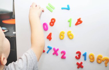 Küçük bir çocuk buzdolabı manyetik numaraları okuyor. Okul öncesi eğitim