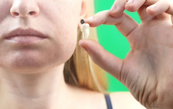 Blurry pose of a woman with toothache and a hand holding the extracted tooth, hocus on the hand