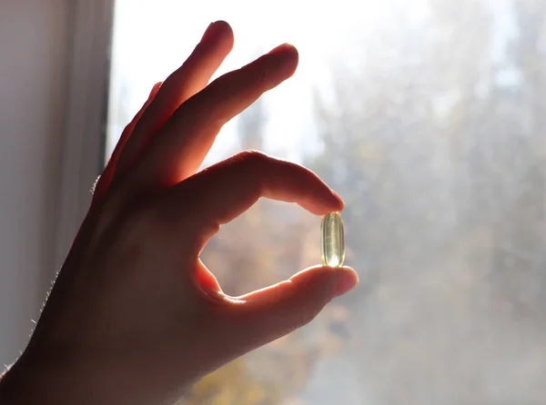 Vitamin D or omega 3 capsules. Vitamin gel in hand against the window. The concept of a lack of vitamin D in the body