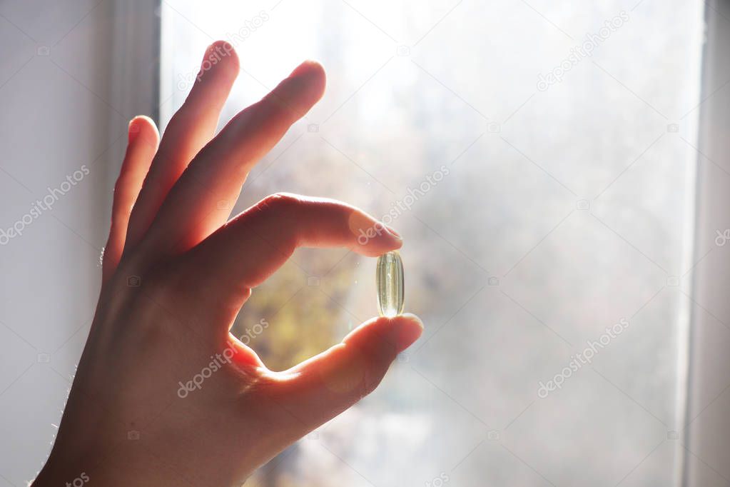 Vitamin D or omega 3 capsules. Vitamin gel in hand against the window. The concept of a lack of vitamin D in the body