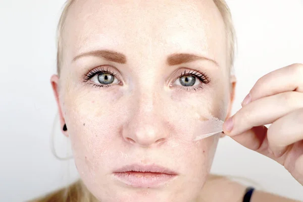 The girl removes the mask film from the face. The concept of removing old dry skin, self-care
