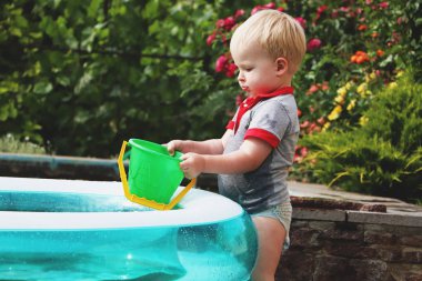 Küçük bir çocuk ile su bir şişme havuz kenarında oynuyor. Yaz ve aile tatil. Mutlu çocukluk