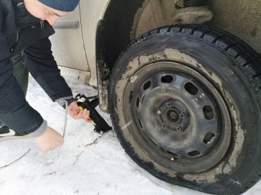 Delikli ve düz lastik yolda. Tekerlek bir jack ile sürücü tarafından yerine