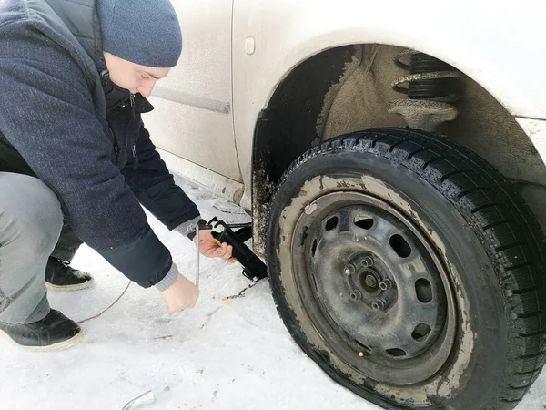 Delikli ve düz lastik yolda. Tekerlek bir jack ile sürücü tarafından yerine