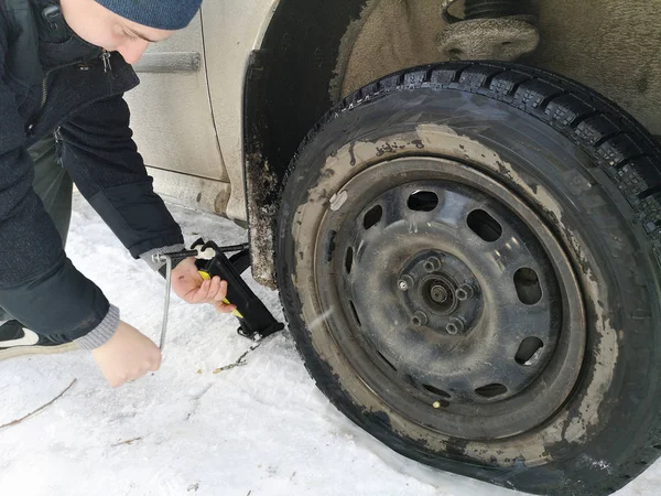 Delikli ve düz lastik yolda. Tekerlek bir jack ile sürücü tarafından yerine