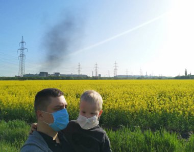 Elinde bir çocuk olan bir adam, bitkinin arka planında tıbbi maskeler takıyor. Çevre kirliliği kavramı, ekoloji