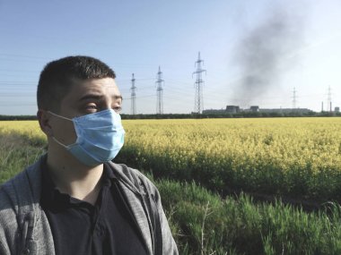 Tıbbi maskeli bir adam, bitkinin arka planına karşı. Çevre kirliliği kavramı, ekoloji