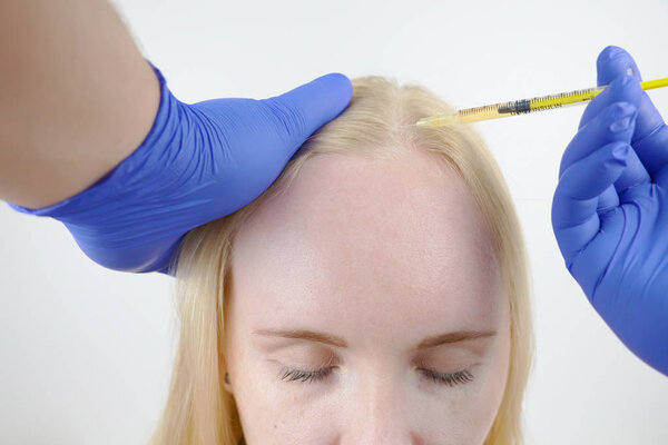 Hair mesotherapy or hair transplant: a beautician doctor makes injections in the head of a woman for hair growth or to prevent baldness