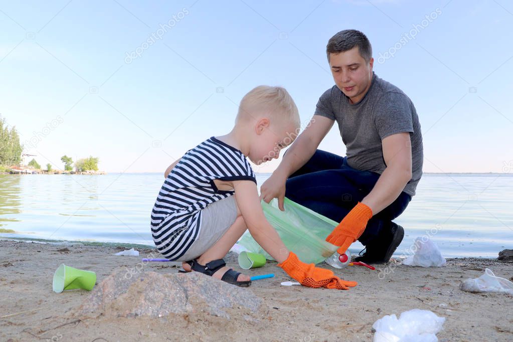 A small child collects trash on the beach. His dad points his finger where to throw garbage. Parents teach children cleanliness. Clean planet concept
