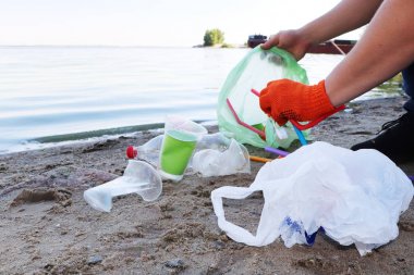 Sahilde çöp toplama. Plastik ve paketler sahile dağılmış. Bir adam plastik toplar. Ekoloji koruma kavramı