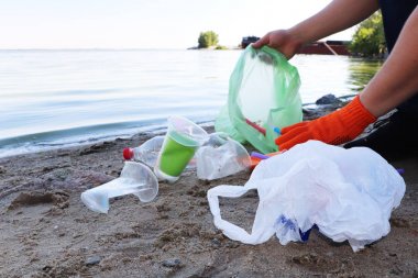 Sahilde çöp toplama. Plastik ve paketler sahile dağılmış. Bir adam plastik toplar. Ekoloji koruma kavramı