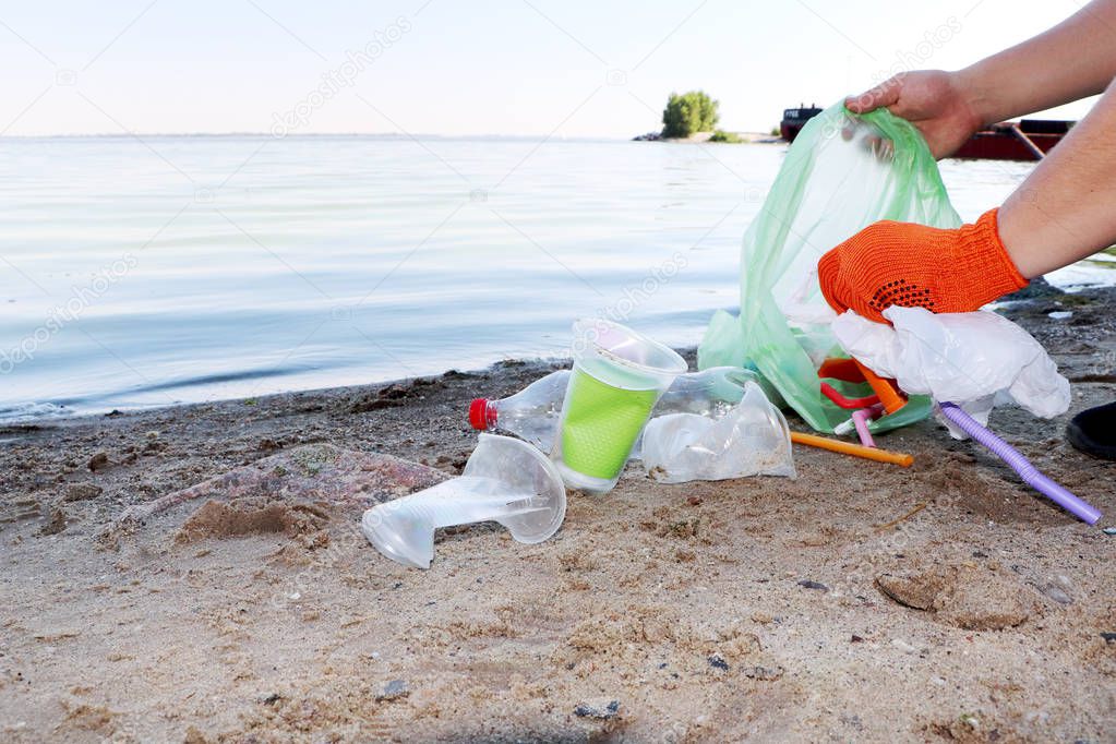 Garbage collection on the beach. Plastic and packages scattered on the beach. A man collects plastic. Ecology protection concept