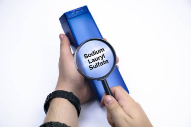 Chemical components on the shampoo label:  Sodium Lauryl Sulfate (sls, sles). A hand holds a blue jar and a magnifier, where the harmful ingredients of a detergent are written in close up. clipart
