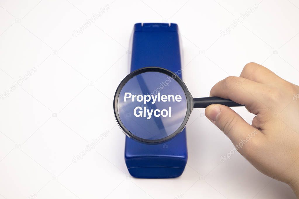 Chemical components on the shampoo label: Propylene Glycol. A hand holds a blue jar and a magnifier, where the harmful ingredients of a detergent are written in close up.