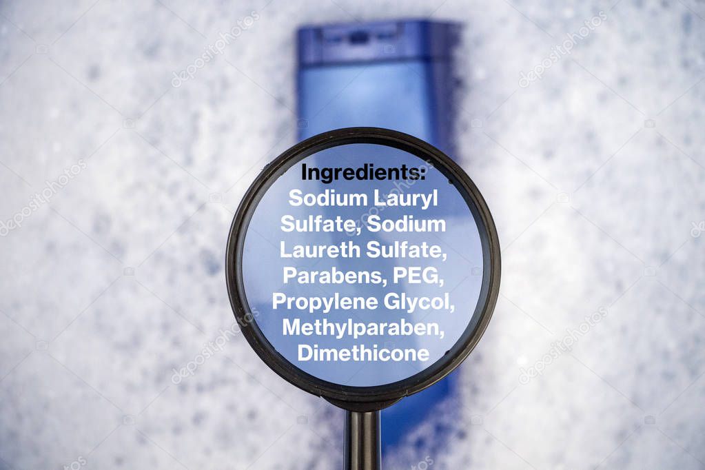 Chemical components on the shampoo label:  Sodium Lauryl Sulfate (sls, sles). A hand holds a blue jar and a magnifier, where the harmful ingredients of a detergent are written in close up.