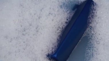 Köpüklü suda mavi bir şampuan konservesi yüzer. Temizlik ve kişisel bakım kavramı.