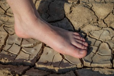 Kadının bacakları çatlamış toprakta duruyor. Ayakların kuru derisi ve nem ve mantar hastalıkları kavramı.