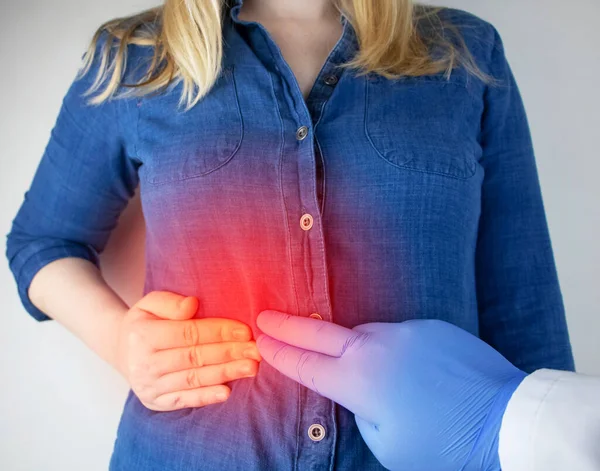 Bir kadın sağ tarafını kaburgalarının altından tutuyor. Karaciğer ağrısı. Karaciğer hastalığında ağrı sendromu. Hepatolojist muayene