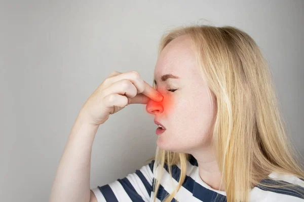 A young woman touches her nose, which is very painful. Medical care concept for difficulty breathing, clogged nasal passages and flu, colds or coronavirus