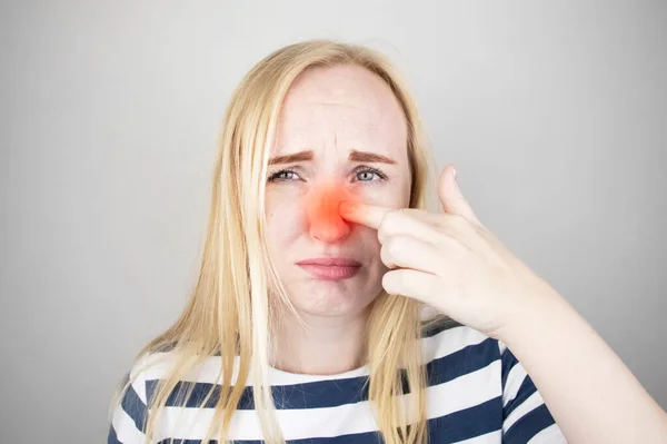 A young woman touches her nose, which is very painful. Medical care concept for difficulty breathing, clogged nasal passages and flu, colds or coronavirus