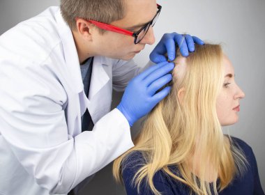Bir doktor trichologist bir sarışının saçı üzerine bir çalışma yürütüyor. Alopecia tedavisi. Saç dökülmesi, alopecia, kaşıntı, kafa yanması, sebora ya da kırılgan son.