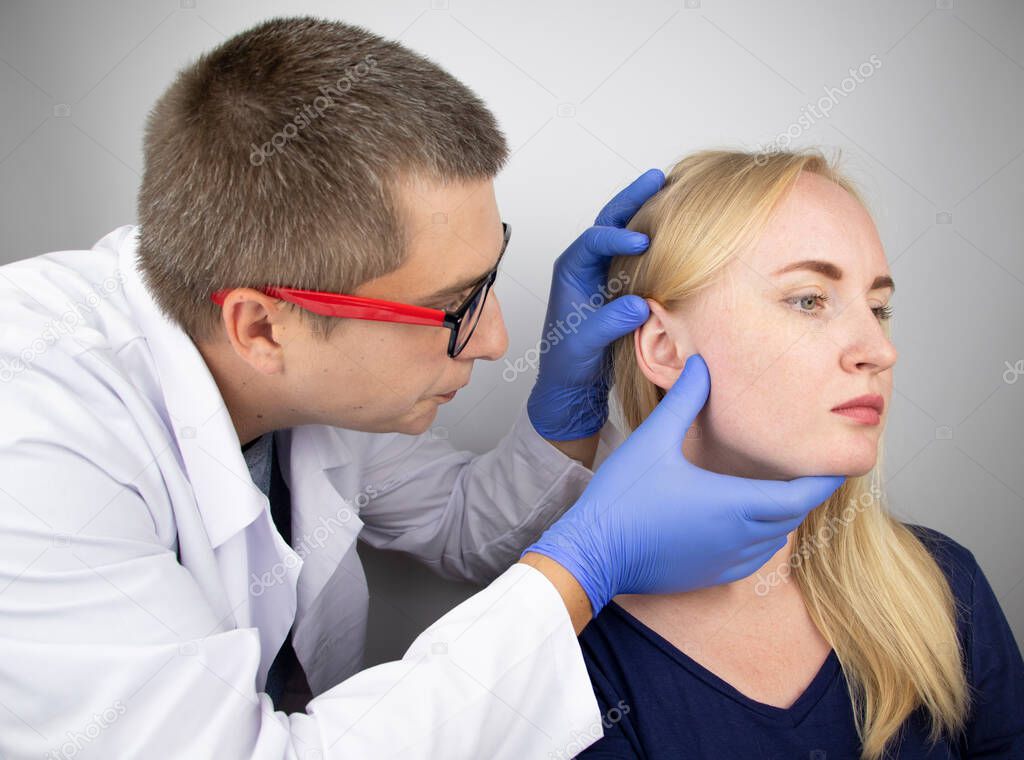 An otolaryngologist examines the ear of a girl who complains of pain. Pain relief and treatment concept. Inflammation of the ear canal or eardrum