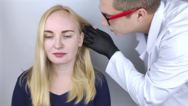 Um médico tricologista realiza um estudo do cabelo de uma loira. Tratamento de alopecia. Perda de cabelo, alopecia, coceira, queimadura na cabeça, seborreia ou extremidades quebradiças — Vídeo de Stock