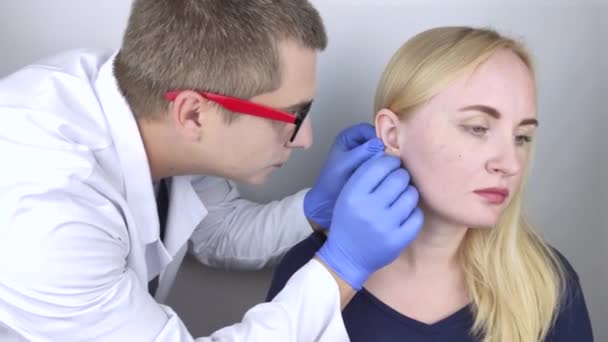 Un otolaryngologue examine l'oreille d'une fille qui se plaint de douleur. Soulagement de la douleur et concept de traitement. Inflammation du conduit auditif ou du tympan — Video