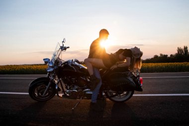 Bisikletli adam ve kadın, dinlenmek ve tutkuyla öpüşmek için yolun kenarında durdular. Gün batımında sevecen motosikletçilerin fotoğrafları. Özgürlük, vahşet ve tutku kavramı.