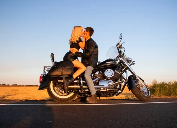 Bisikletli adam ve kadın, dinlenmek ve tutkuyla öpüşmek için yolun kenarında durdular. Gün batımında sevecen motosikletçilerin fotoğrafları. Özgürlük, vahşet ve tutku kavramı.