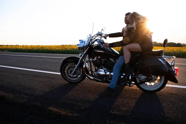Bisikletli adam ve kadın, dinlenmek ve tutkuyla öpüşmek için yolun kenarında durdular. Gün batımında sevecen motosikletçilerin fotoğrafları. Özgürlük, vahşet ve tutku kavramı.