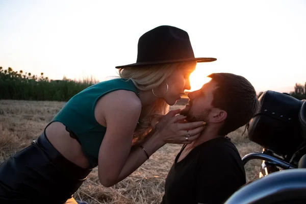 Bikers man and woman stopped at the side of the road to rest and kiss passionately. Photos of loving motorcyclists at sunset. The concept of freedom, brutality and passion