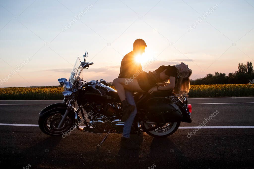 Bikers man and woman stopped at the side of the road to rest and kiss passionately. Photos of loving motorcyclists at sunset. The concept of freedom, brutality and passion