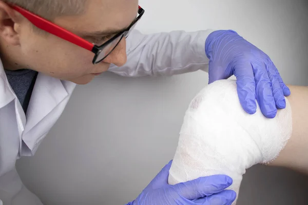 The doctor bandages the knee of a girl who is injured. Stopping bleeding by applying a pressure bandage to the injury. First aid for injuries. The technique of applying a cruciform bandage.