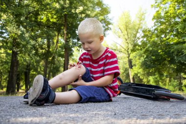 Dört yaşında bir çocuk motosikletten düştü ve dizini kırdı. Babam yarayı dezenfekte ederek ve yara bandı uygulayarak ilk yardımı sağlıyor..